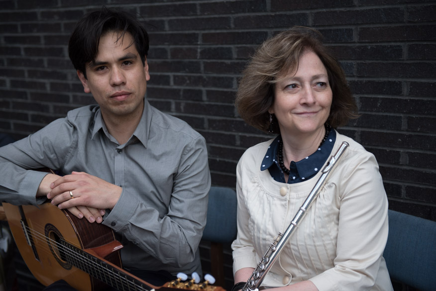 Musicians seated together, one with a guitar and the other with a flute